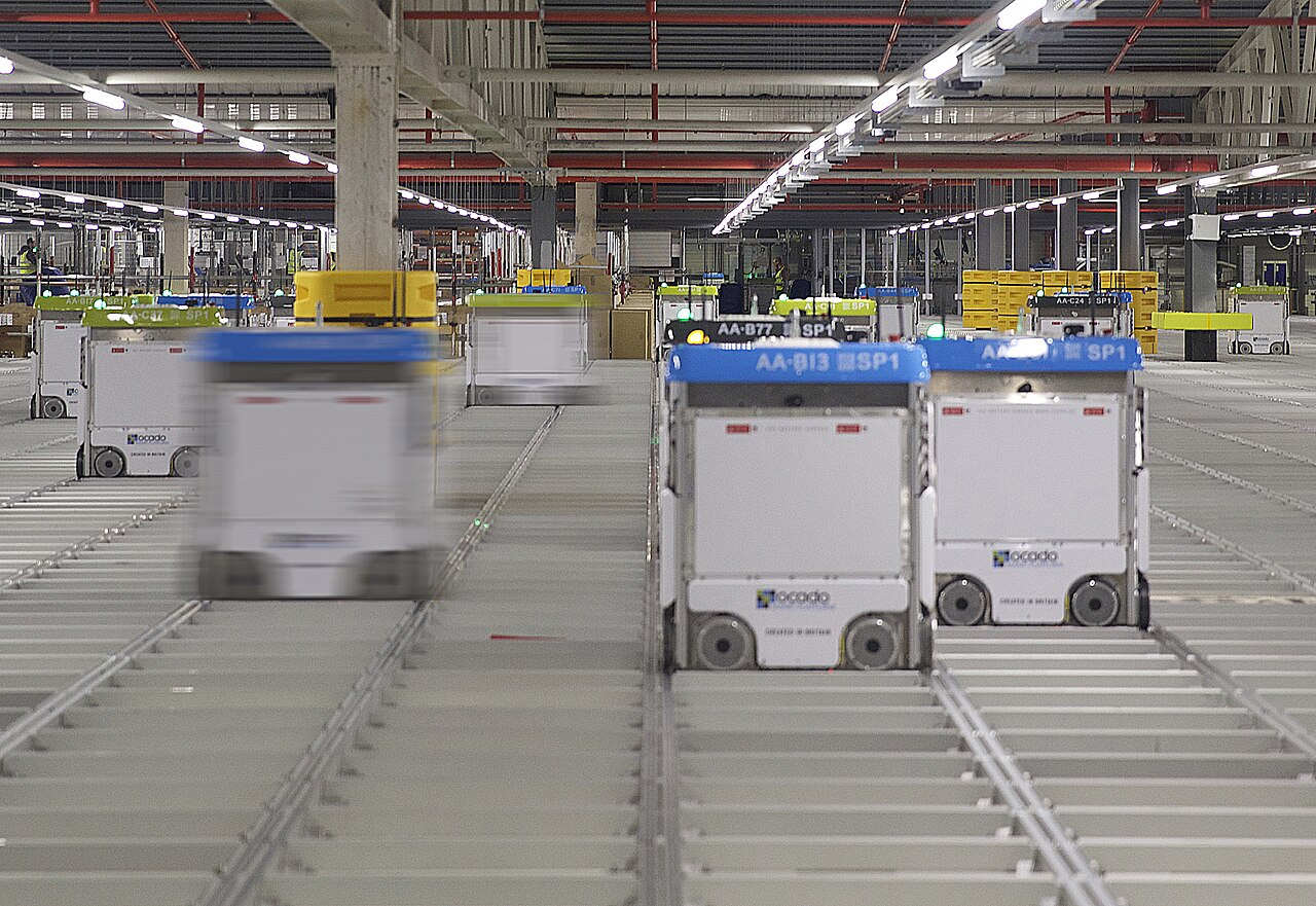 Hệ thống robot Ocado di chuyển trên lưới kim loại trong kho tự động hóa, mỗi robot mang logo ocado và mã định danh