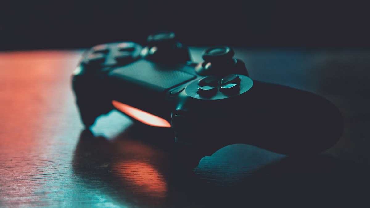 Tay cầm PlayStation DualShock trên mặt bàn gỗ trong ánh sáng xanh cam
