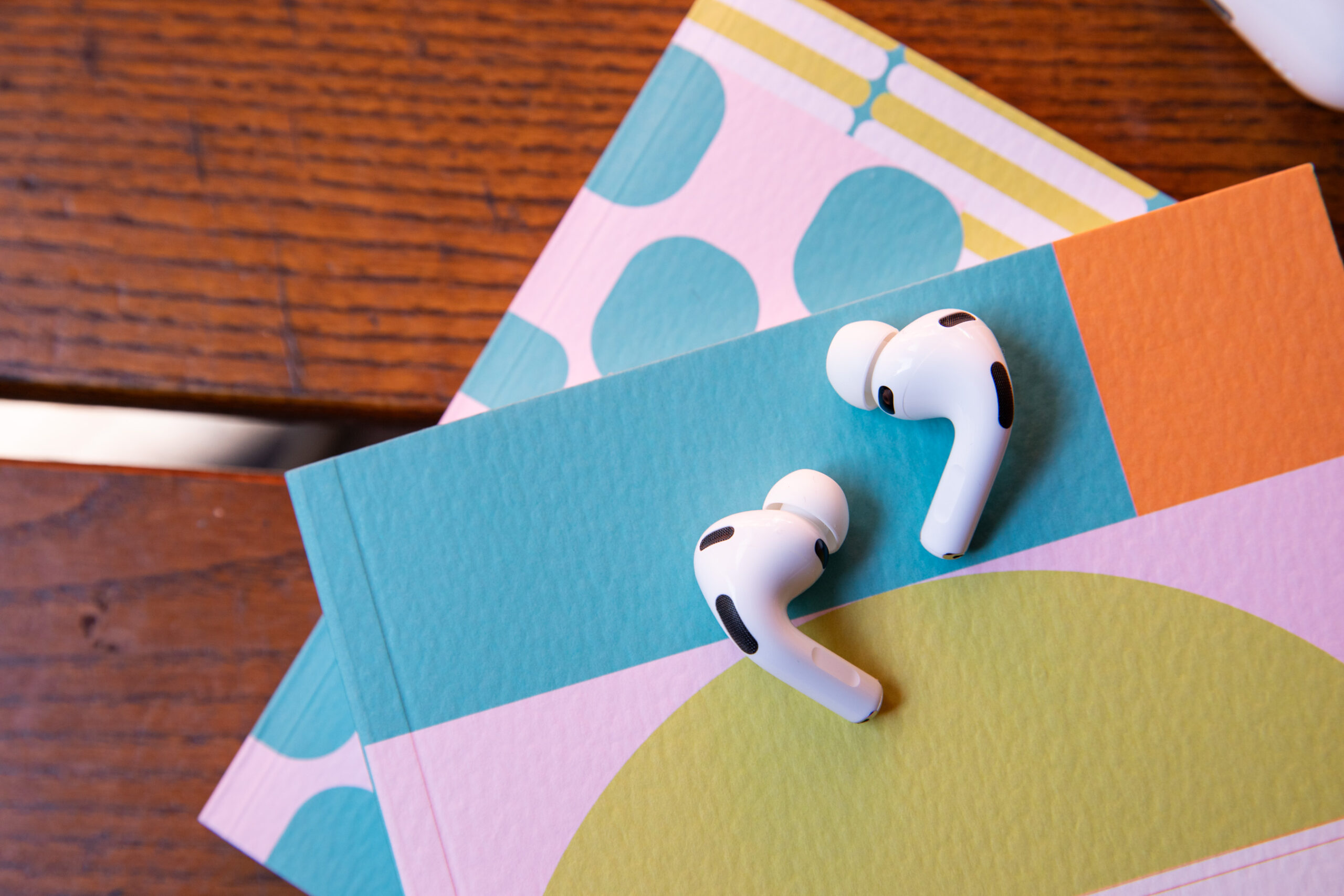 AirPods Pro 3 màu trắng đặt trên cuốn sổ tay họa tiết màu pastel trên bàn gỗ