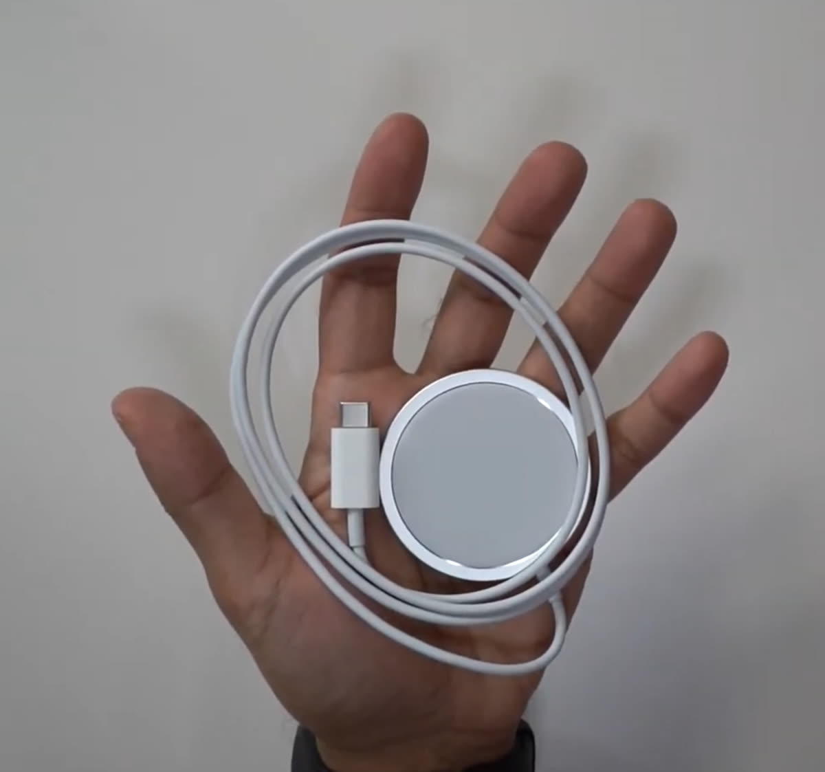 Bàn tay cầm bộ sạc không dây MagSafe tròn với cáp USB-C của Apple