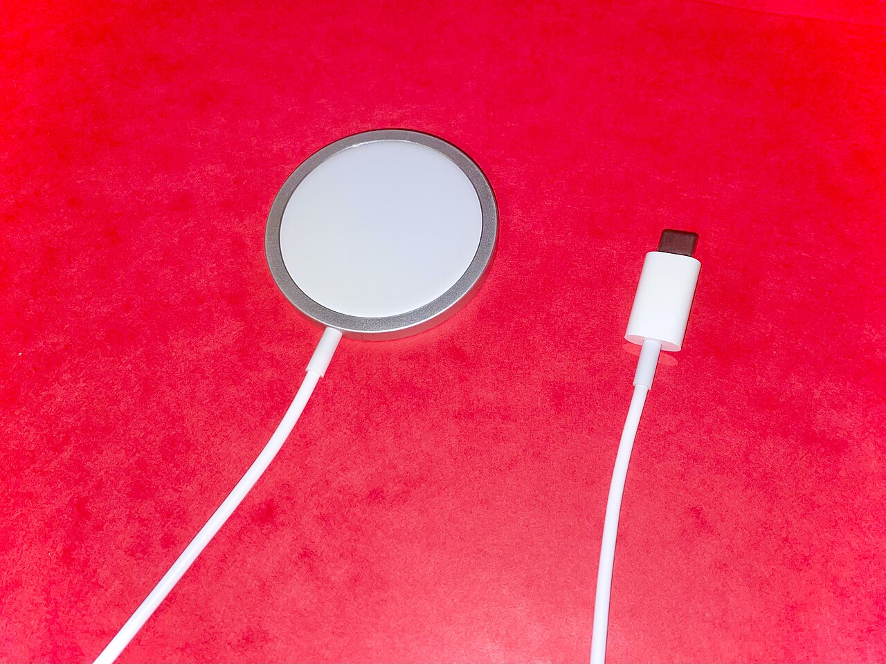 Bộ sạc MagSafe đế tròn màu trắng với dây cáp Lightning trên nền đỏ