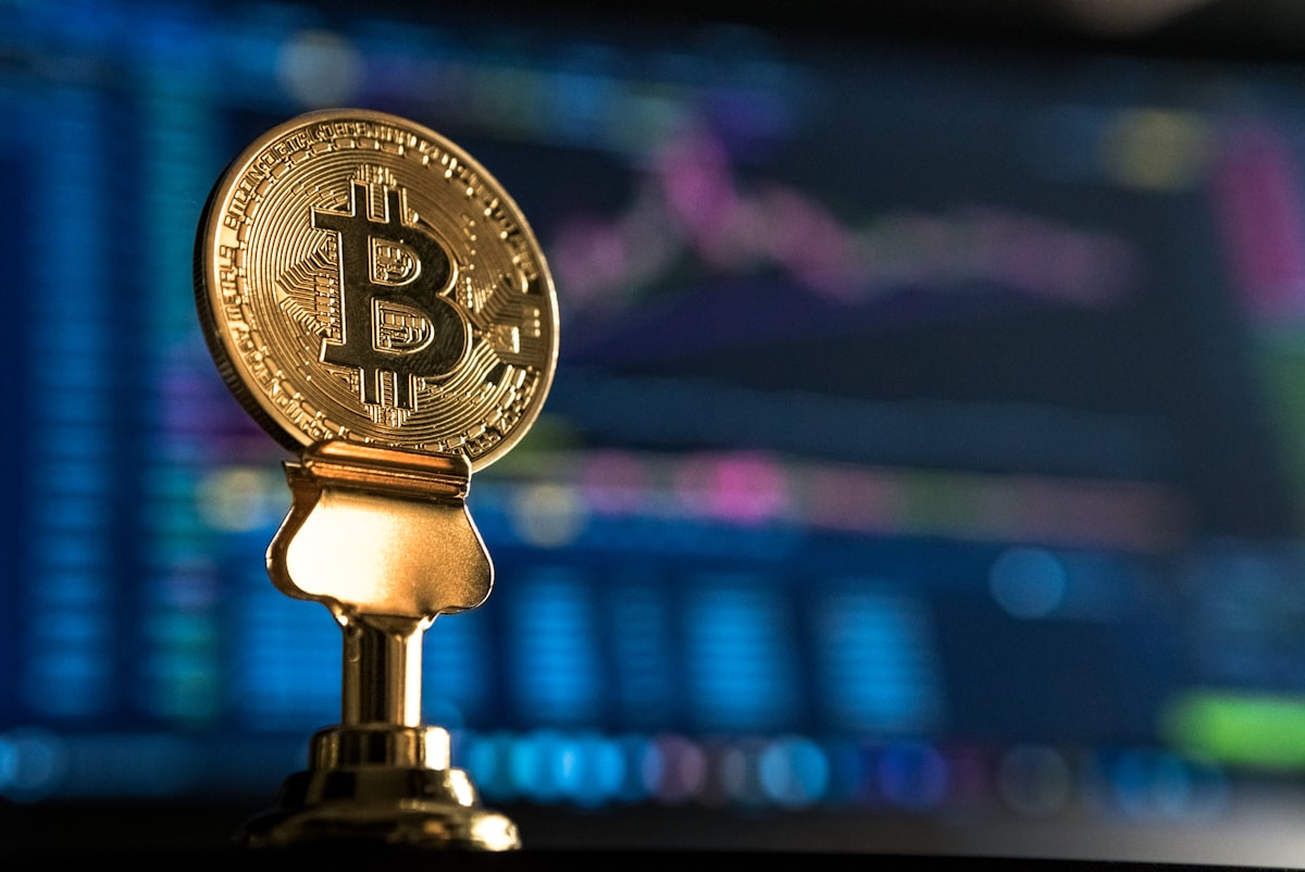Đồng xu Bitcoin vật lý trên giá đỡ kim loại với biểu đồ giá màn hình