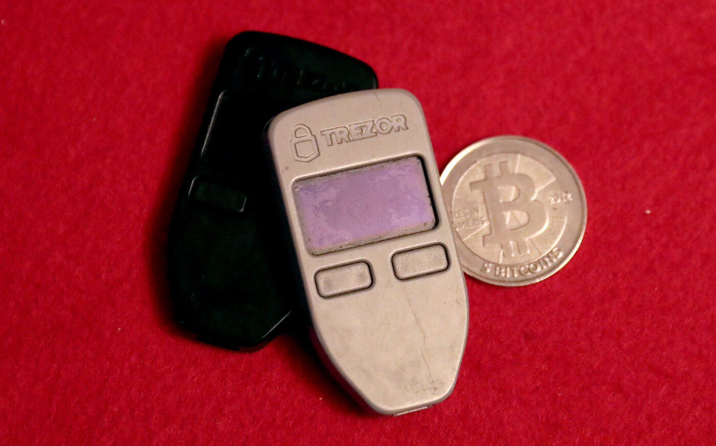 Ảnh thực tế hai ví cứng Trezor One đặt cạnh một đồng Bitcoin vật lý, thiết bị lưu trữ seed và khóa riêng tư ngoại tuyến
